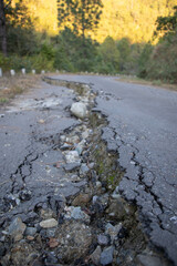 A winding road is severely damaged with cracks in the asphalt due to recent geological activity....