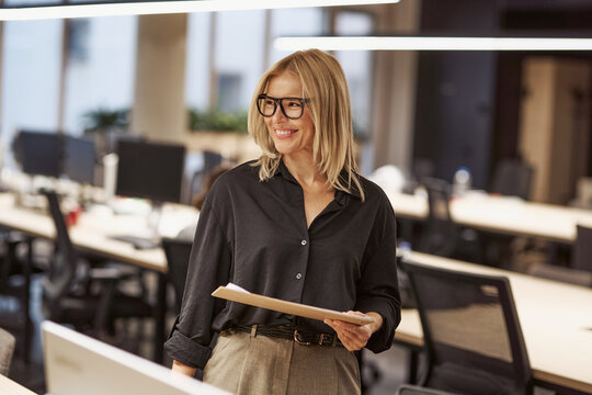 A Smiling Businesswoman in a Modern Office with Clipboards and a Focused Attitude
