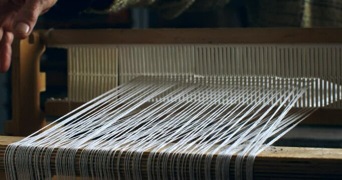 Super slow motion close up of female artisan skillfully working with woven weaving machine, using threads or yarns to craft cloth textile piece in her workshop studio at 1000 fps. 