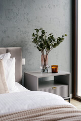 Bedside table with candle and home decor next to neatly made bed