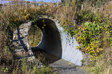 Circular corrugated iron and stone tunnel underpass and gravel track of a rural mountain bike trail...