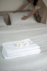 plumeria flower and towels on the bed in the luxury hotel room ready for tourist travel and Hands of the hotel maid clean the bedroom