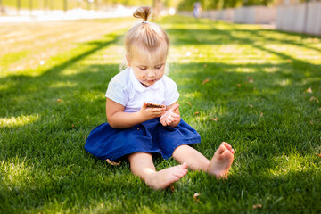 little blonde girl in school uniform sitting or lying on the grass eating delicious sweet cookies