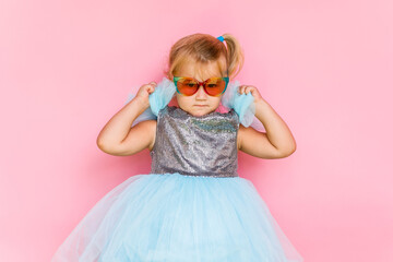 Girl with long hair in festive paper hat and dressy dress on pink background tossing gold confetti