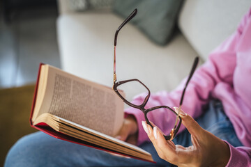 unknown woman sit on sofa read book and hold eyeglasses