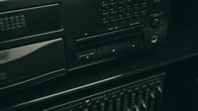 A tray with a compact disc is inserted into the CD player and a hand presses the play button in a hi-fi music center. Closeup. Macro. Shallow depth of field. Shot in motion