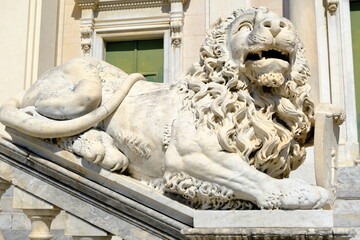 Ligurian city. Sculpture of a lion with a mane.White marble statues in front of the Basilica of Santo Stefano in the Ligurian town. Italy