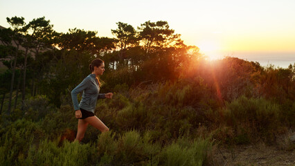 Woman, morning and running in forest at sunset for fitness on trail for exercise, training and workout. Endurance, nature and athlete in outdoor sports for practice for wellness and health in woods