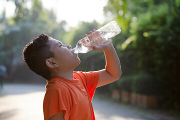Boy drinking water from a bottle at a public park.