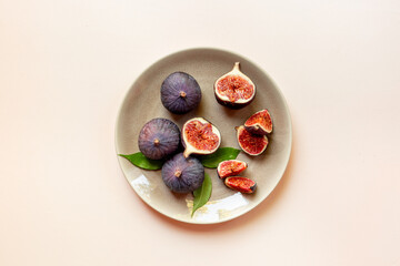 Plate with fresh ripe figs whole and slices with green leaves on white background. Top view