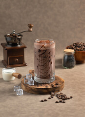 Iced Mocha: A glass of Iced Mocha with chocolate drizzle, served on a wooden board with ice cubes and coffee beans. A milk jug and coffee grinder add to the scene.