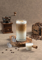 Iced Cappuccino: A tall glass of Iced Cappuccino with frothy milk, served with ice cubes, coffee beans, and a small milk jug. A coffee grinder and beans complete the scene.