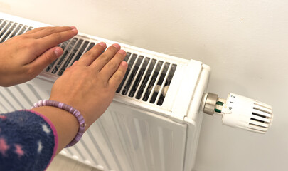 The child's hands warm their hands near the heating radiator. Saving gas in the heating season.
