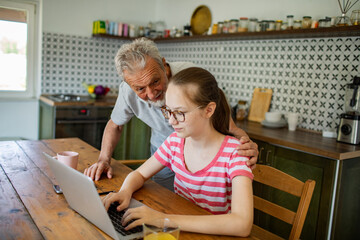 Grandfather helping granddaughter with homework on laptop