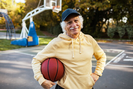 Portrait of a senior man holding basketball on outdoor park court