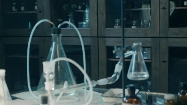 A large old style chemistry lab with lots of beakers, test tubes, flasks, spirit lamps, chemicals and other chemical equipment on a large glass table. Closeup. Macro. Shot in motion