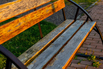 A weathered wooden bench under warm sunlight in a quiet park setting during late afternoon.