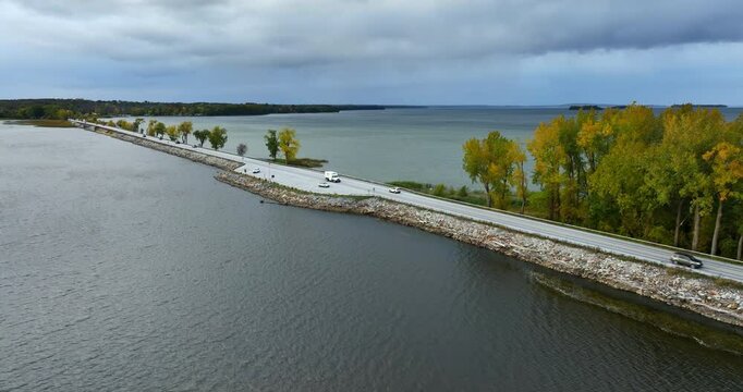 Cars riding by the highway built along the lake. Waterscape of Lake Champlain, Vermont, New England, USA. Grey day on the lake.