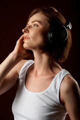 Fototapeta premium Beautiful girl with short haircut in a white T-shirt listening to music with headphones and posing in a studio on a black background