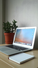 Fototapeta premium A white laptop computer with a blank notebook and a potted plant on a wooden desk.