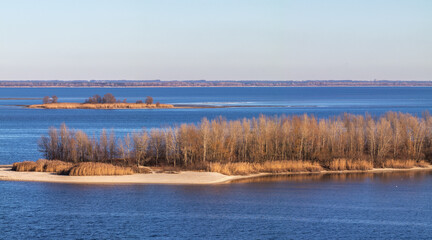 Islands emerging from wide river under blue sky