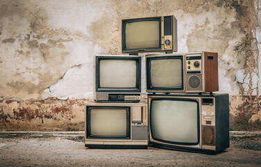 Retro old televisions pile on floor in front of old brick wall. Antique and vintage style photo,...