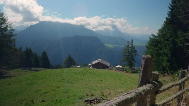 Cozy cabin nestled in a grassy mountain valley with breathtaking views of distant peaks and lush forests.