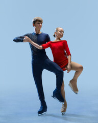 Two young, elegant figure skaters in perfect sync, executing complex pose on ice against cold blue...