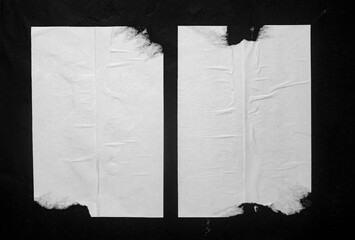 Two white torn posters on a black wall.