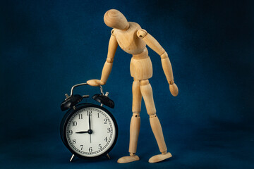 Wooden mannequin of a man looking at the alarm clock dial. Conceptual photo.