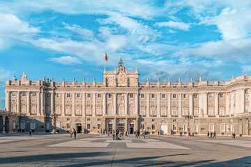 The Royal Palace of Madrid stands majestically under a bright blue sky, its neoclassical facade...