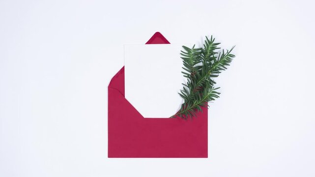 Spruce branch appears from a red envelope with a white sheet. Merry Christmas and Happy New Year concept. Greeting Card. White background. Template for text. Copy space.