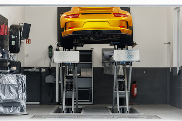 Sport luxury car raised on hydraulic lift perform diagnostics inspection at maintenance station. Automobile repair and check up at workshop garage. DIY self service oil and tyre change box rental