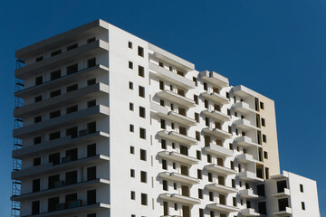 Block of flats under construction with a white facade. Raw apartment building structure without windows. New property development. Apartment purchase background. Unfinished investment.