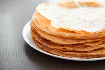 A round dish with fried pancakes on a brown table. A sweet dessert for breakfast. Sunny morning.