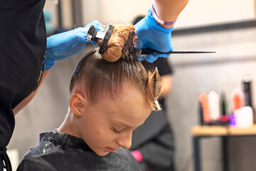 stylist in blue gloves makes a slicked-back hairstyle with a high bun for a girl before a...