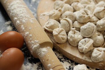 Raw dumplings, selective focus. Cooking pelmeni, flour, eggs and wooden rolling pin. Meat pelmeni or ravioli on wooden board, dark table. Slavic traditional dish. Food background
