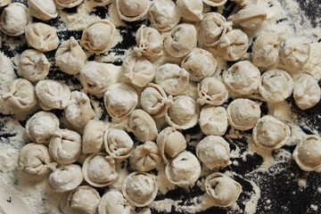 Raw dumplings, top view, flat lay. Cooking dumplings. Meat dumplings or ravioli on dark background. Slavic traditional dish. Food background. Dumplings rolled in flour