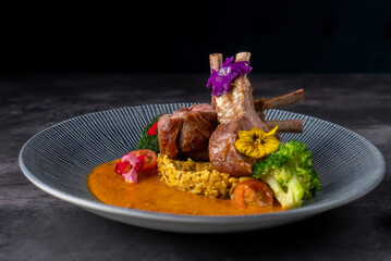 Beautifully plated dish of lamb chops garnished with edible flowers, accompanied by colorful...