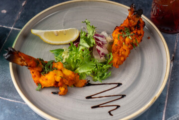 Two vibrant, orange-hued shrimp, garnished with fresh herbs, alongside a crisp salad and a wedge of lemon. a drizzle of sauce adds a decorative touch.