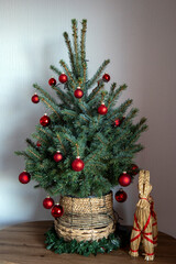 A Scandinavian-inspired Christmas display featuring a red-decorated artificial tree in a straw pot, accompanied by a traditional Yule Goat.