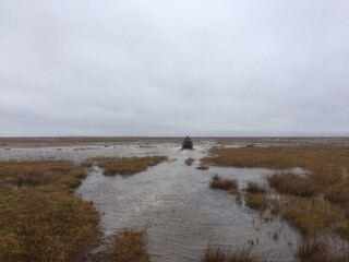 Wet, dreary and flat landscape in fall colours with a stream flowing through with an ATV in the foreground, near Arviat, Nunavut, Canada