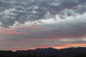 A scenic view of a landscape at sunset unfolds like a creative work, with dark hills silhouetted against a sky filled with clouds