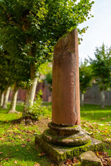 A weathered stone column stands tall in a grassy park, surrounded by trees on a sunny day