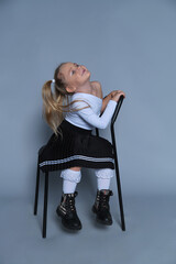 Fototapeta premium This playful image shows a 5-year-old girl in a trendy outfit sitting on a chair, laughing joyfully in a studio setting. Her vibrant personality and stylish look make this perfect for children's