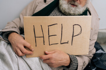 Closeup cropped shot of unrecognizable aged homeless man sitting on cold city sidewalk, holding...