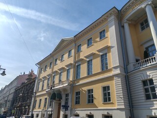 Naklejka premium grand yellow building with symmetrical windows and classical detailing, featuring a decorative arched entrance. The clean facade highlights the elegance of traditional urban architecture under a clear