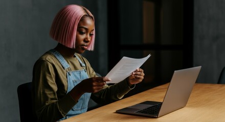 Obraz premium Focused young woman with pink hair reviewing documents at laptop in home office.