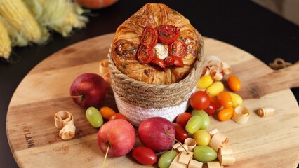 astry with roasted tomatoes rests in natural woven basket, colorful tomatoes, red apples, and wooden curls scattered around, placed on wooden surface creating an eco-friendly display.