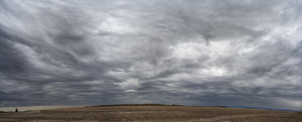 Panorama of grey storm clouds above flat dry farm fields. Many shades of gray.
